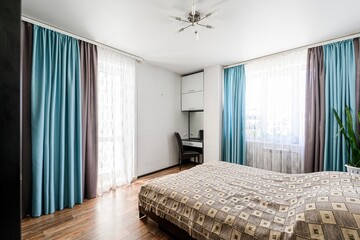 Cozy bedroom with bed, teal and brown curtains, white walls, and wooden floor. A vanity table and...