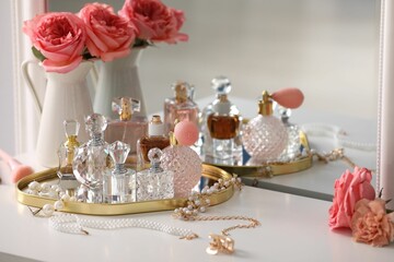 Bottles of different perfumes, accessories and flowers on dressing table indoors