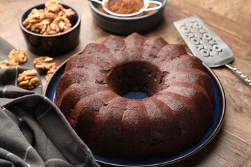 Tasty chocolate bundt cake, walnuts and cocoa powder on wooden table, closeup