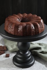 Tasty bundt cake and pieces of chocolate on grey table, closeup