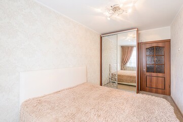 bedroom features a bed with a beige furry blanket, a mirrored closet, and a wooden door. The wallpaper has a subtle floral pattern