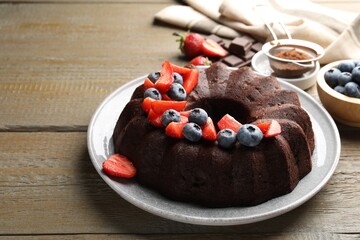 Tasty chocolate bundt cake with berries on wooden table. Space for text