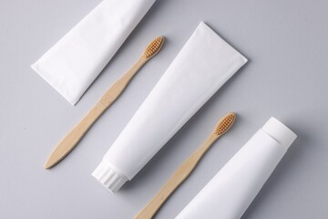 Tubes of toothpaste and toothbrushes on light grey background, flat lay