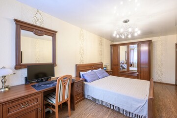 cozy bedroom with wooden furniture, featuring a bed, desk with a computer, wardrobe with mirrors, and a chandelier