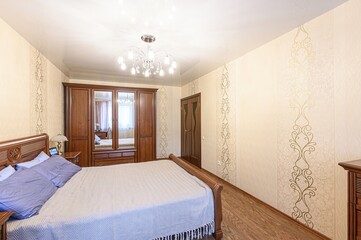 Cozy bedroom with a wooden bed, wardrobe with mirrors, patterned wallpaper, and a decorative chandelier