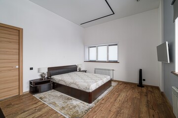 Bright bedroom features a large bed, wooden floors, white walls, and a window with blinds. Modern...