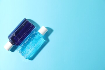 Bottles of mouthwash on light blue background, top view. Space for text
