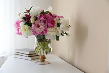 Bouquet of beautiful peonies and books on white table indoors. Interior design
