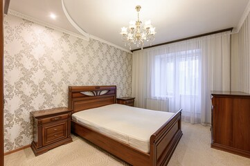 Cozy bedroom with a wooden bed, nightstands, and dresser. Floral wallpaper and a chandelier add a classic touch
