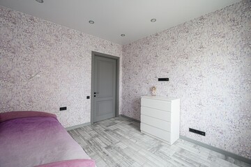 bright room with floral wallpaper, a gray door, and light wood floors. A white dresser stands...