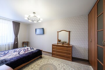 cozy bedroom featuring a bed with a patterned cover, a wooden dresser with a mirror, a wall-mounted...