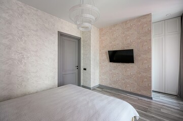 modern bedroom featuring textured walls, a gray door, a chandelier, a TV, and a bed with a...