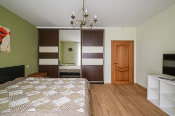 bedroom interior featuring a large bed, a sliding door wardrobe with a mirrored panel, a wooden...