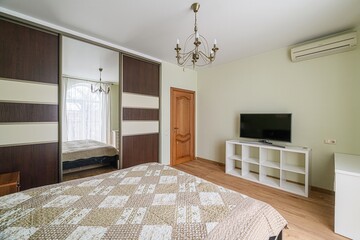 bedroom features a bed with a patterned quilt, a sliding door wardrobe with a mirror, a TV on a...