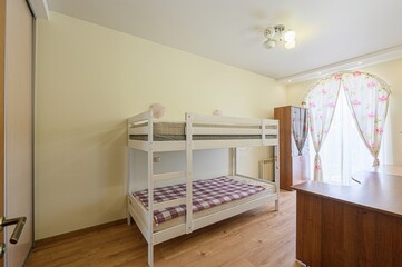 cozy room with a white bunk bed, light yellow walls, and a window with floral curtains. Wooden...