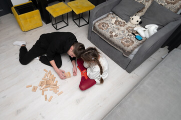 Playing together on a cozy floor in a modern living room with a game of wooden blocks as laughter...
