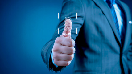 A close-up photograph of a hand wearing a dark business suit making a thumbs up gesture against a blurred dark blue background