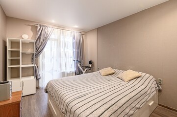 cozy bedroom with a bed, striped blanket, and pillows. A window with curtains is on the left, and a...