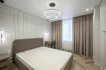 modern bedroom with a bed, nightstand, curtains, and a unique circular chandelier. Neutral tones create a calm and inviting space