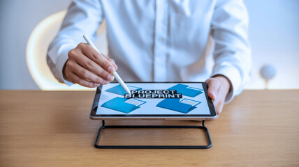 A close-up photograph of hands using a tablet device with a stylus. The tablet is propped up on a black stand and displays floating blue folder icons against a white background