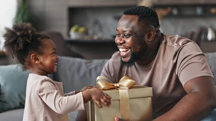 African American little daughter handing gift box to father in modern living room