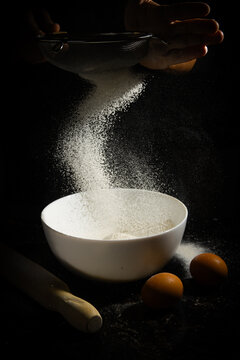 Tamizado de harina en cuenco blanco con huevos y rodillo en fondo negro