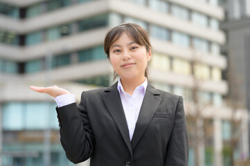 片手を横に出してポーズをとるスーツ姿の女性が柔らかく微笑む春の一枚