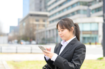 スマートフォンを両手で持って立ち止まりながら操作するスーツ姿の女性