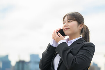 スマートフォンを使って話すスーツ姿の新入社員が遠くを見つめる姿