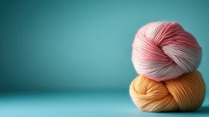 A charming display of two soft yarn balls in pink and yellow shades stacked atop a turquoise surface, inviting creativity and sophistication in craft-making.
