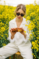 Woman enjoying a croissant in a yellow flower field during daytime