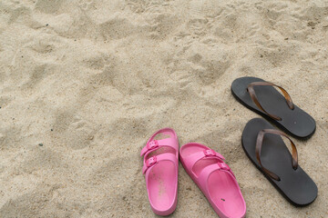 
A pair of pink sandals and black flip-flops rest on a sandy beach.