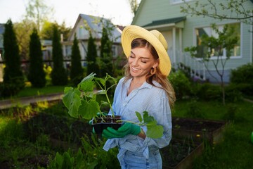 Portrait of a smiling gardener woman standing next to her green garden holding a young seedlings...