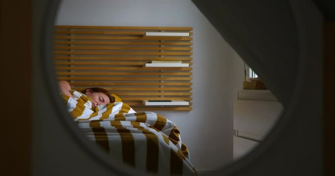 A woman reflected in a mirror is in her bedroom bed sleeping, in the morning. The alarm clock on her mobile phone rings and she wakes up and picks it up. In the morning. Light comes in through the win
