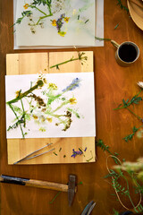 Top view of DIY botanical art project with wildflower prints on paper, rustic wooden table, natural craft materials, and creative floral composition