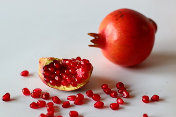 Pomegranate. Open fruit with glistening ruby red arils on a white surface, captured in soft natural light