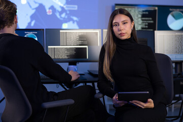 Confident female Cybersecurity Analyst or Manager in large Cyber Security Operations Center SOC...
