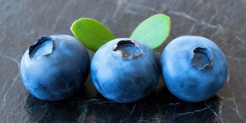 Three ripe blueberries sit on a dark, textured surface, perfect for a healthy snack.