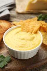 Tasty cheese dipping sauce in bowl and nacho chips on table, closeup