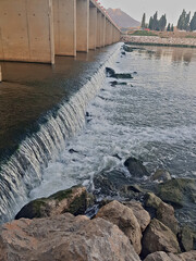 a wide waterfall flows beneath a bridge in the center of a wadi.