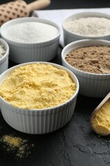 Different types of flour in bowls on black textured table, closeup