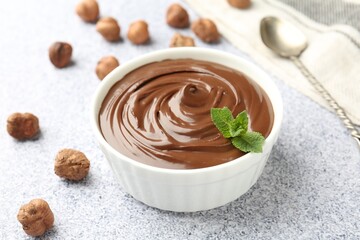 Tasty chocolate spread with mint in bowl and hazelnuts on grey textured table, closeup