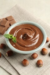 Tasty chocolate spread, pieces, mint and hazelnuts on light table, closeup
