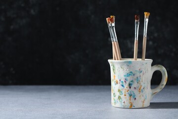 Brush with color paints in cup on grey table. Space for text