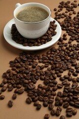 Aromatic coffee in cup and beans on beige background, closeup