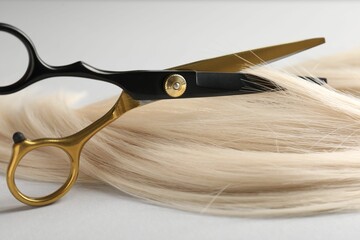 Cutting blonde hair lock with scissors on light grey background, closeup