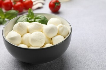 Tasty mozzarella cheese balls, tomatoes and basil on light grey table, closeup. Space for text