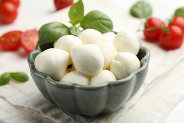 Tasty mozzarella cheese balls, tomatoes and basil on white wooden table, closeup