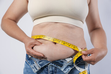Overweight woman measuring her belly with tape on light background, closeup