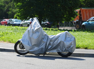 Motorcycle covered with a cover standing near the lawn, Dybenko Street, Saint Petersburg, Russia, June 20, 2025